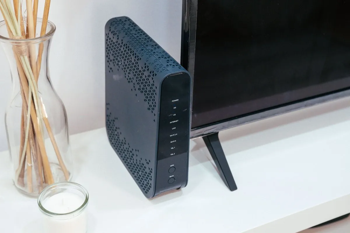 A dark Wi-Fi router standing next to a TV on a white shelf.